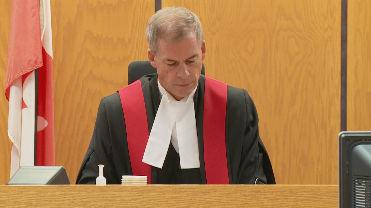 Man with grey hair wearing black and red judicial robe looks down at his desk.