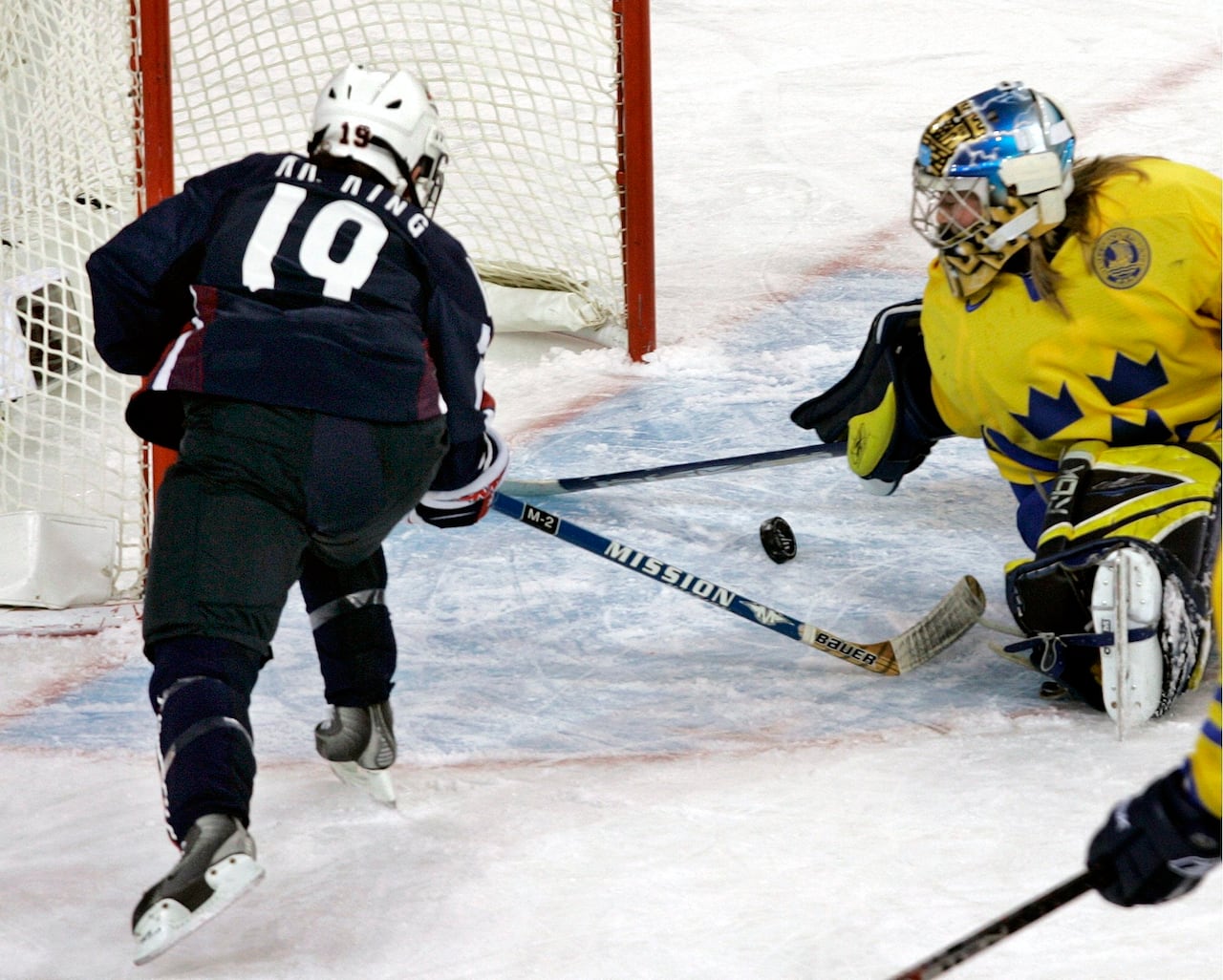 A hockey player shoots on a goaltender.