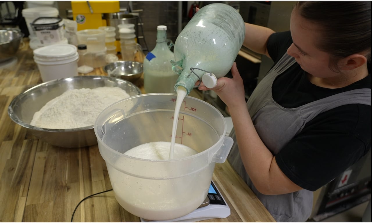 A jug of frothy liquid is being poured into a larger container.
