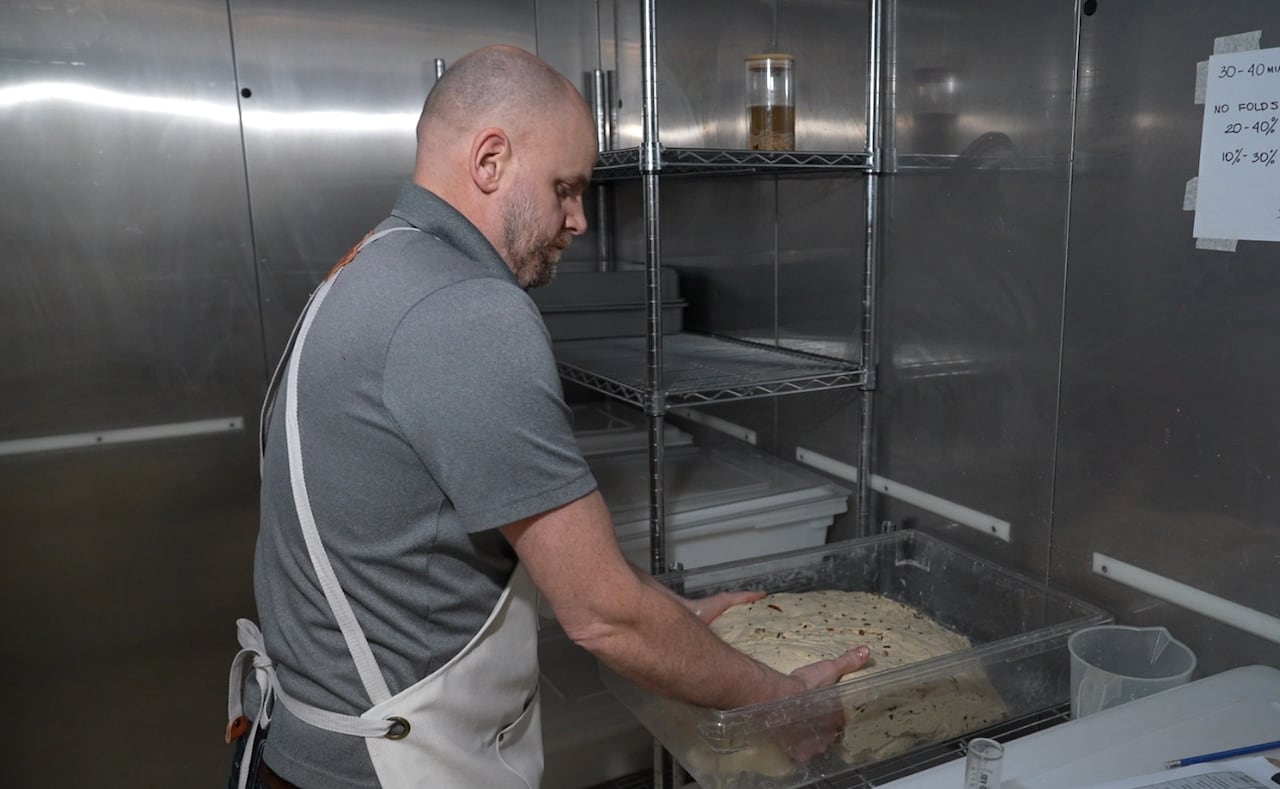 A man in an apron folds a large chunk of dough.