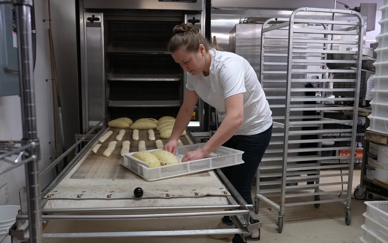 A woman loads bread onto an oven sheet to bake.