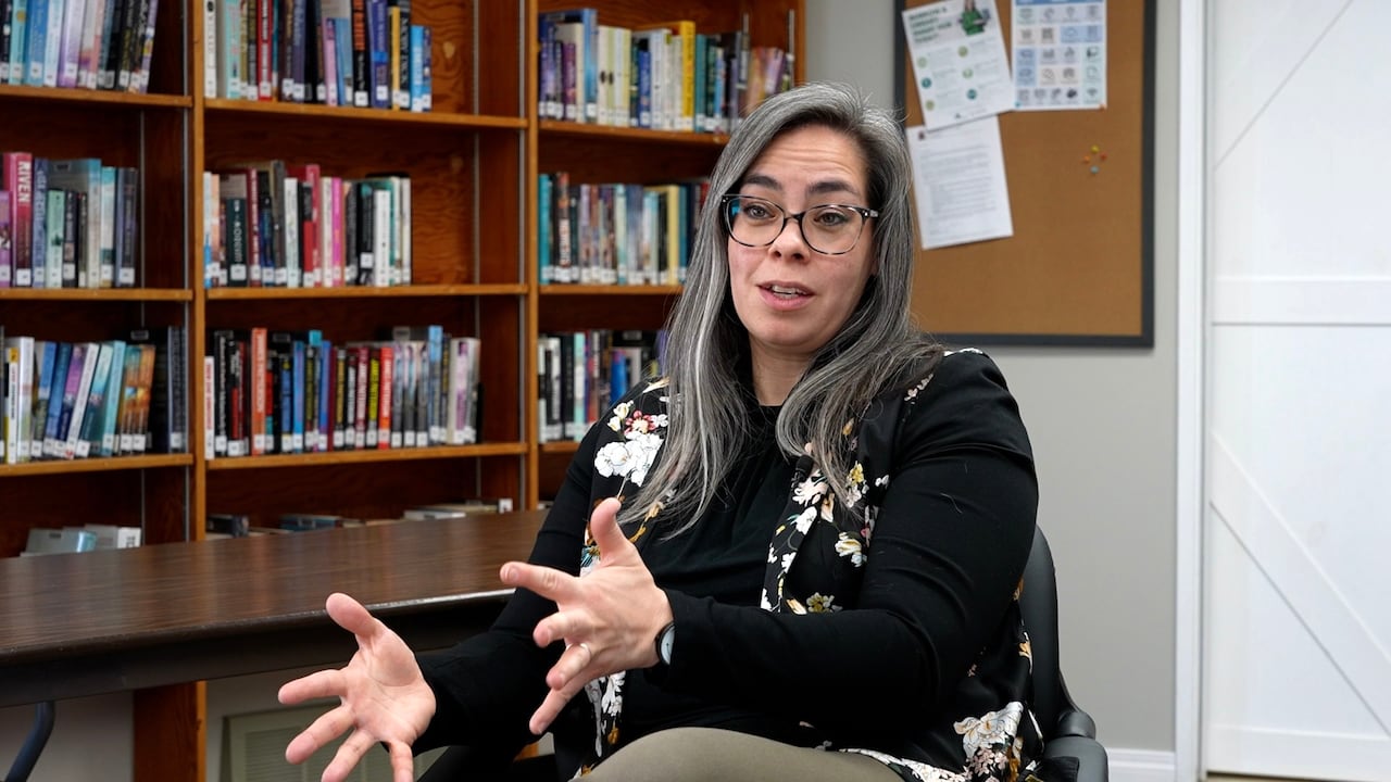 Woman talking across with a bookshelf in the background.