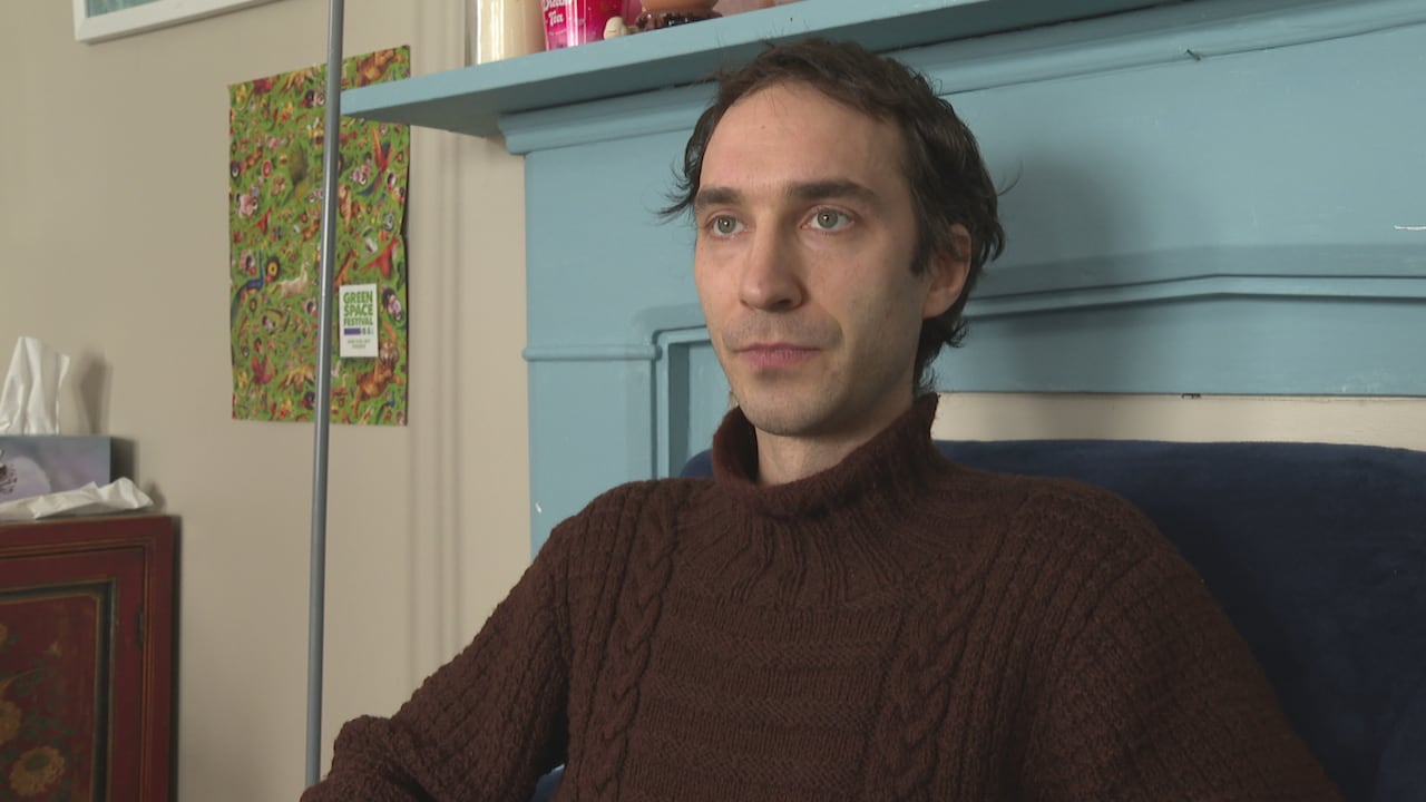 Man in brown sweater sits in front of a light-blue mantle.