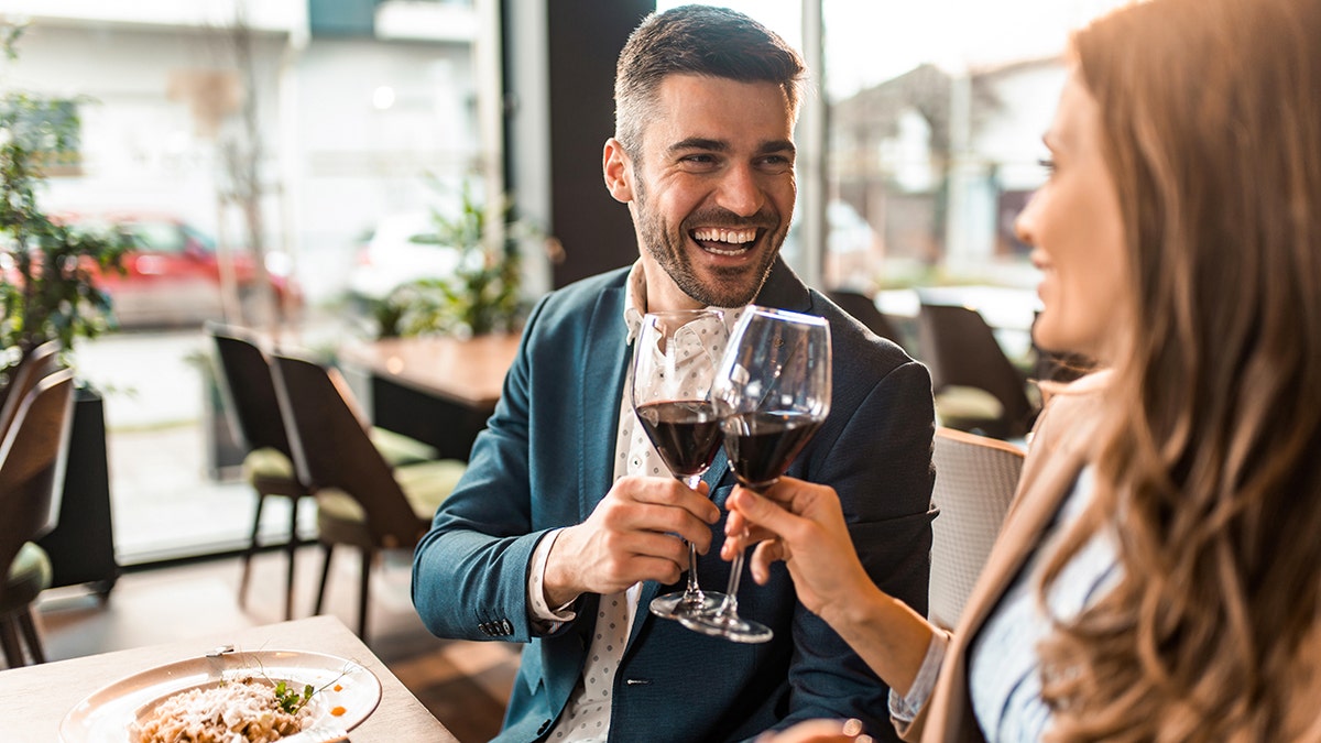 man and woman cheers wine glasses at dinner