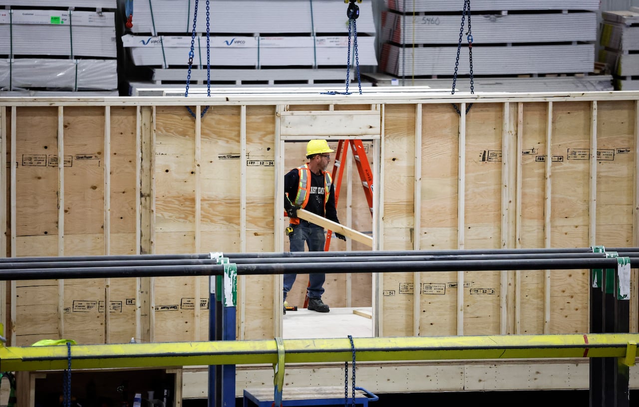 A worker in a safety vest and hard hat carrying work through a modular home.