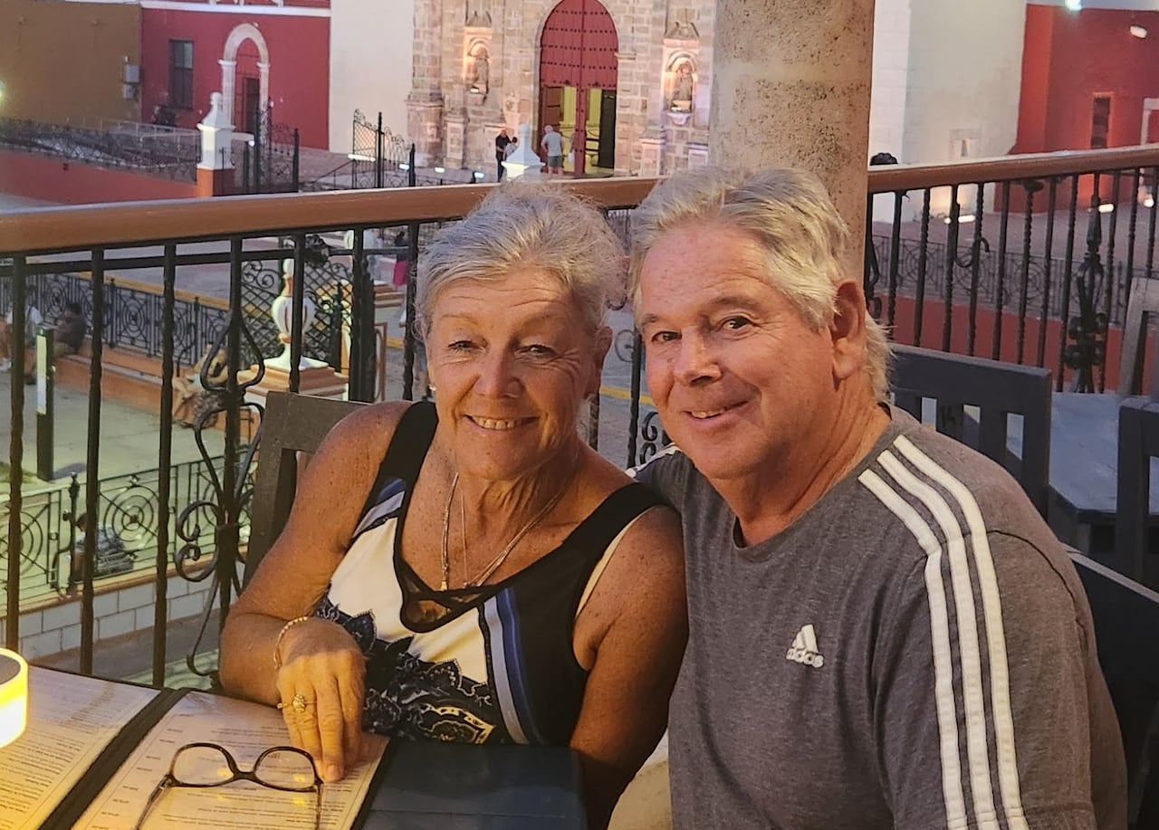 A woman and man sit at a restaurant table on a patio overlooking a historic building.