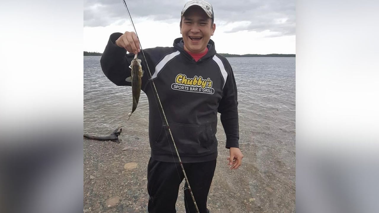 A person is seen holding a fish outside by the water.