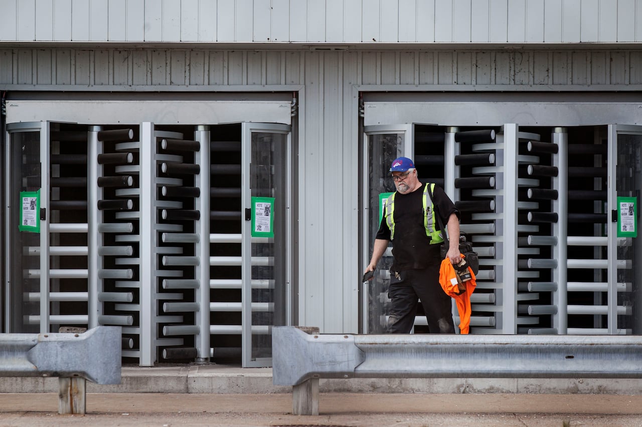 Photo showing a man wearing black clothes and a reflective vest standing outside a factory.