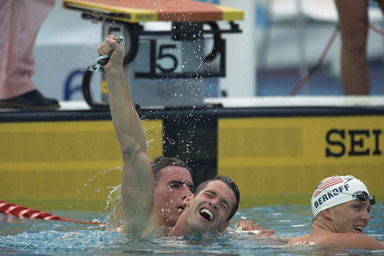 A man in a swimming pool raises his arm in triumph.