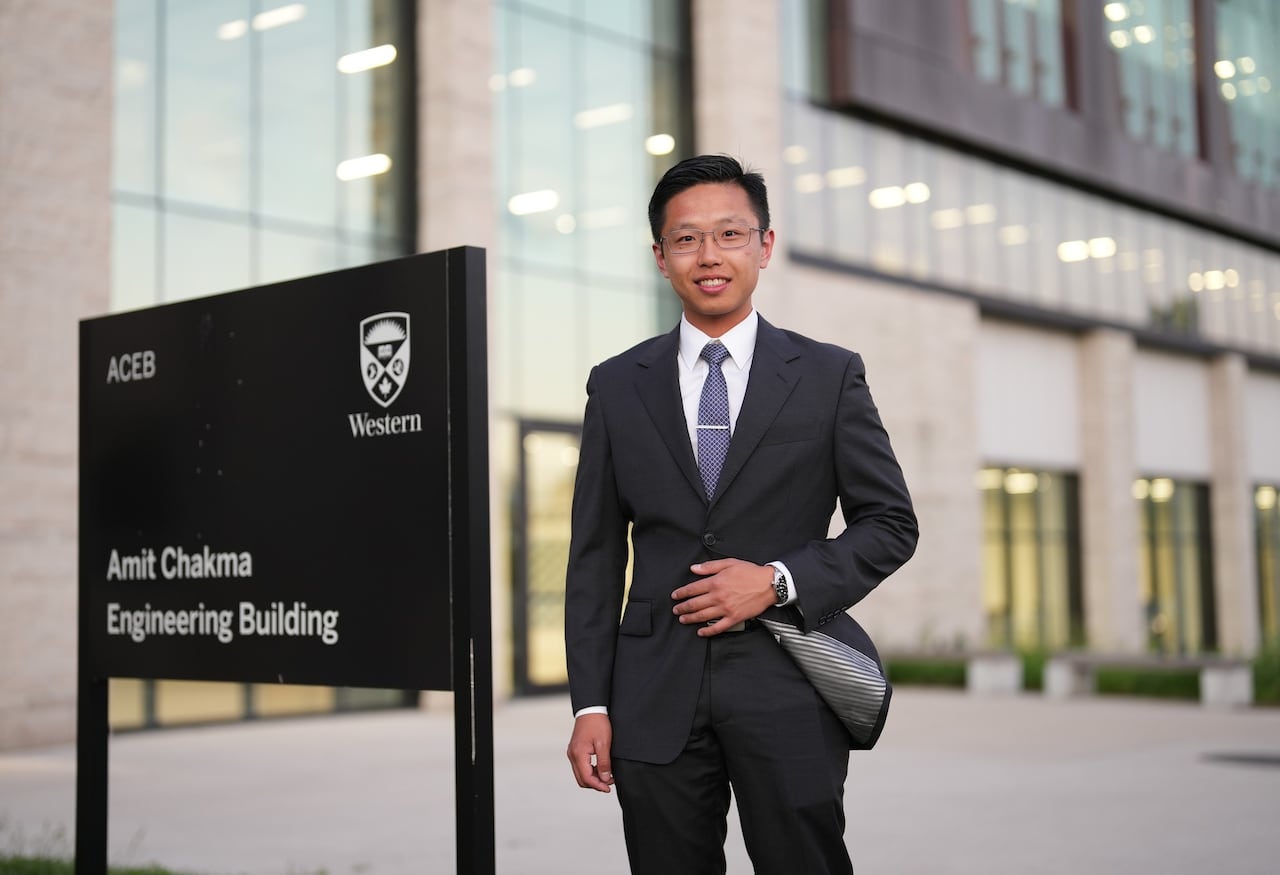 A man in a suit smiles next to a sign for the Amit Chakma Engineering Building with a Western logo on it.