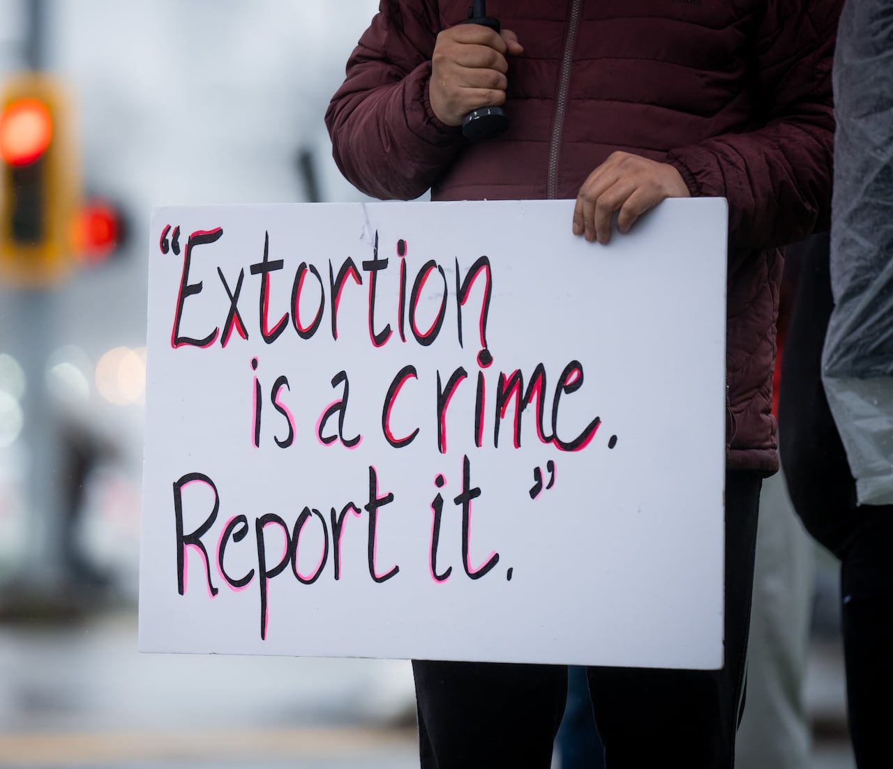 A person holds a sign reading 'Extortion is a crime. Report it'