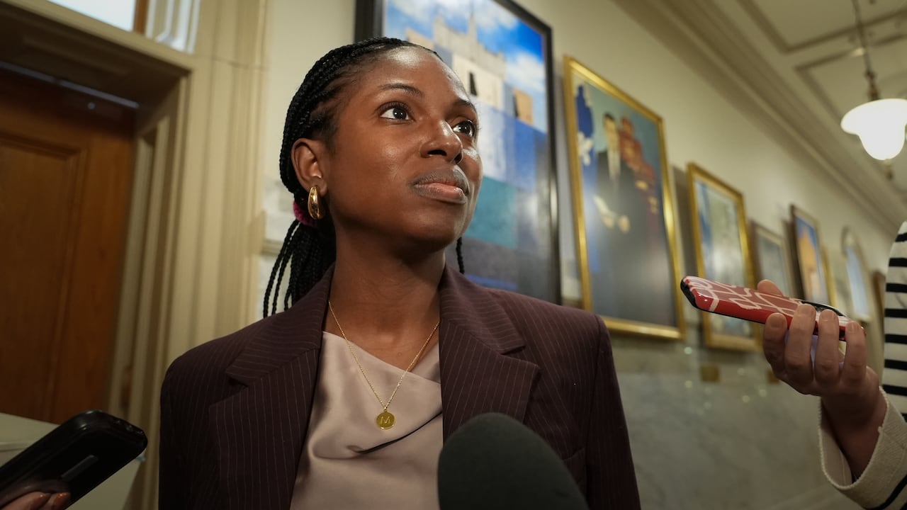 A woman stands in front of cameras and microphones.