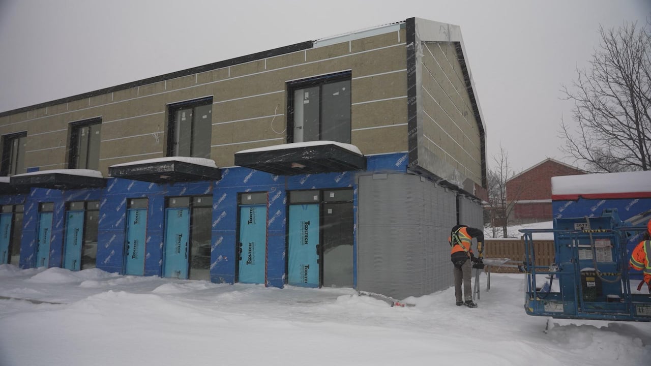 A worker in a high-visibility vest works outside on a townhome complex under construction in snowy weather.