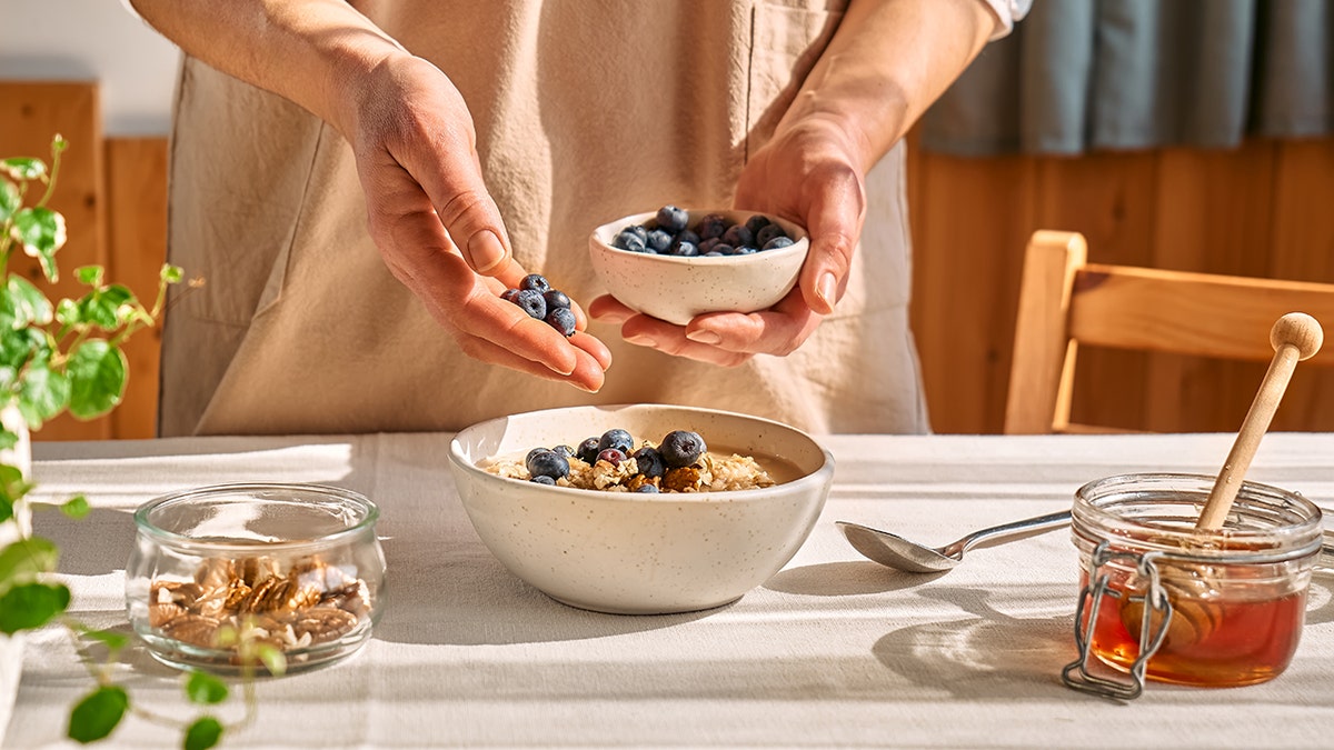 Person adding blueberries to oatmeal.