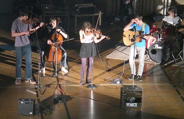 Teens playing instruments at a pep rally in a gymnasium.