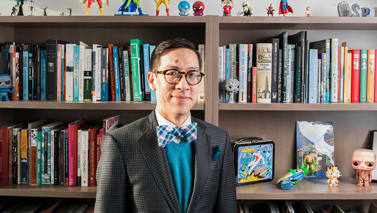 Man in suit and  bow tie standing in front of a bookshelf filled with books.