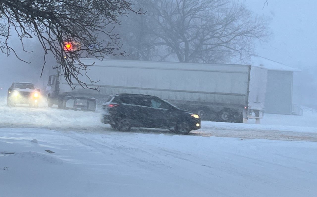 A semi truck and other vehicles on a road in a snow storm.