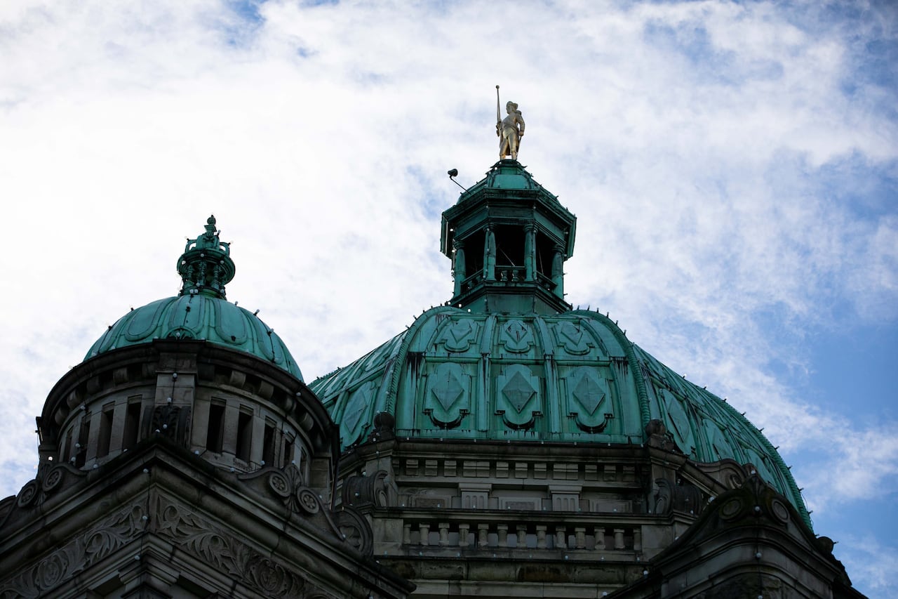 The exterior of a legislature building with blue domes and a golden statue.