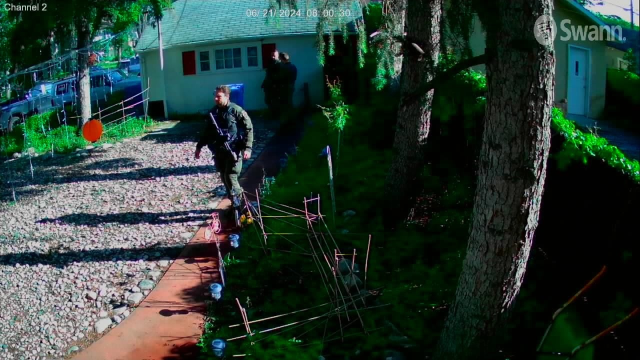 Police officer with a rifle walking through a backyard 