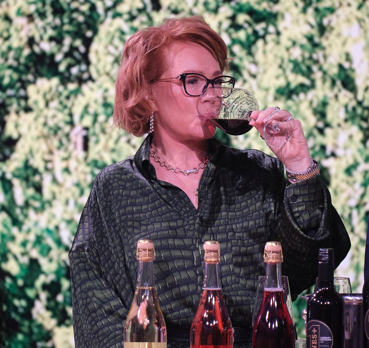 A woman with red hair drinks from a glass of red wine.