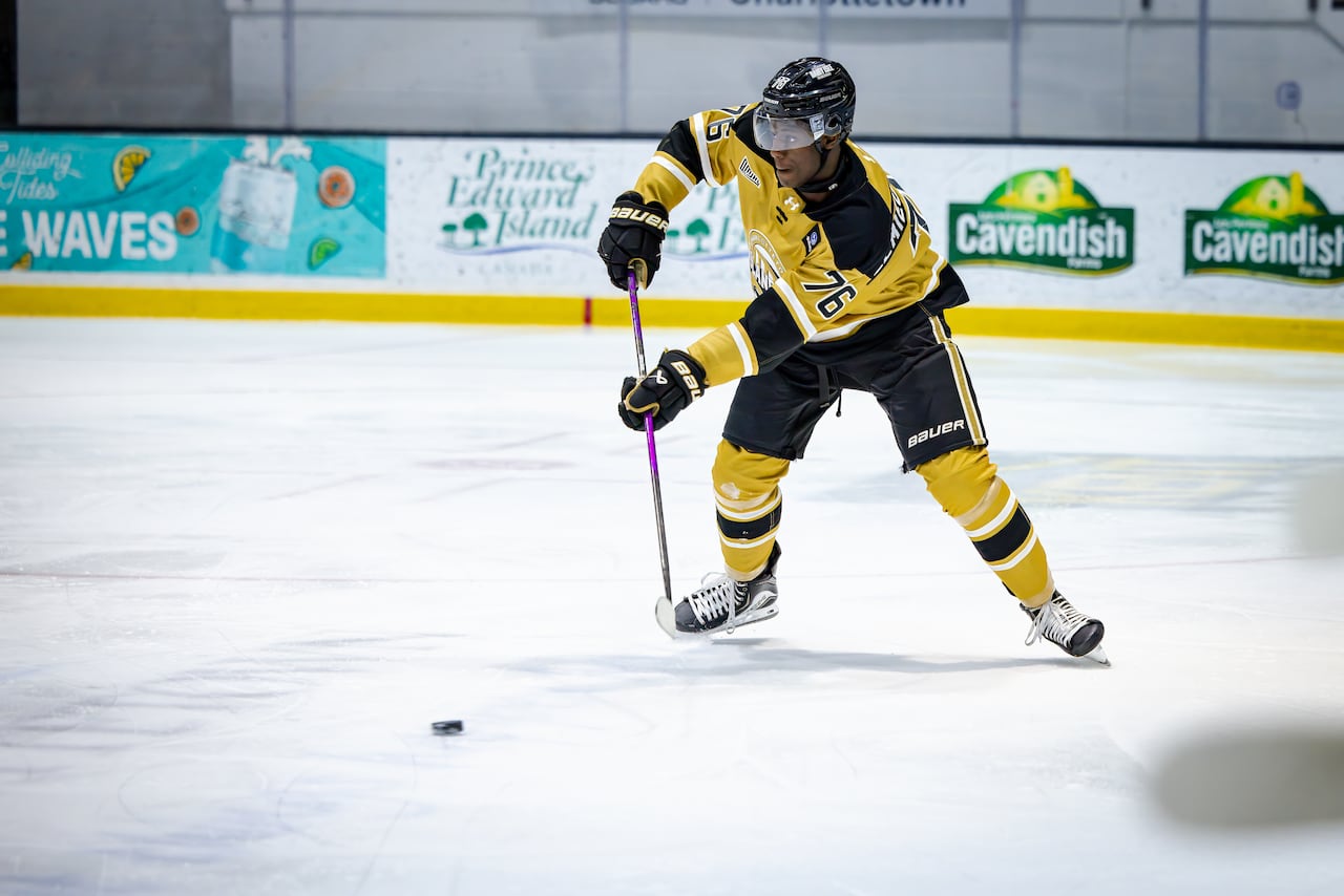 Hockey player in yellow jersey holds purple stick out towards the puck. 