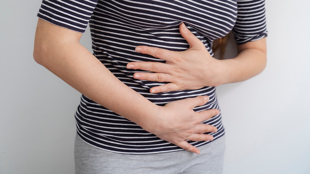 Woman's midsection seen as she clutches her abdomen in pain.