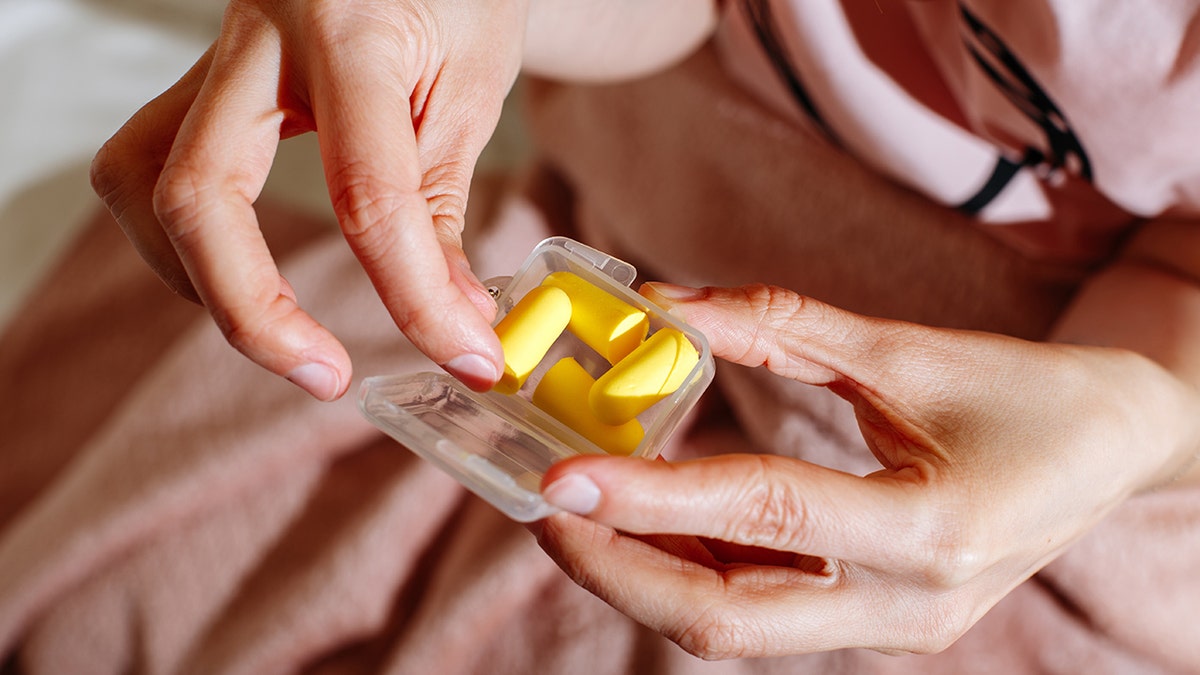 woman takes yellow foam earplug from plastic container
