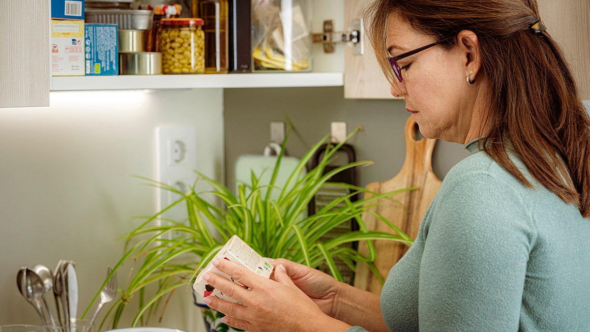 Portrait of a woman in kitchen reading label of food package