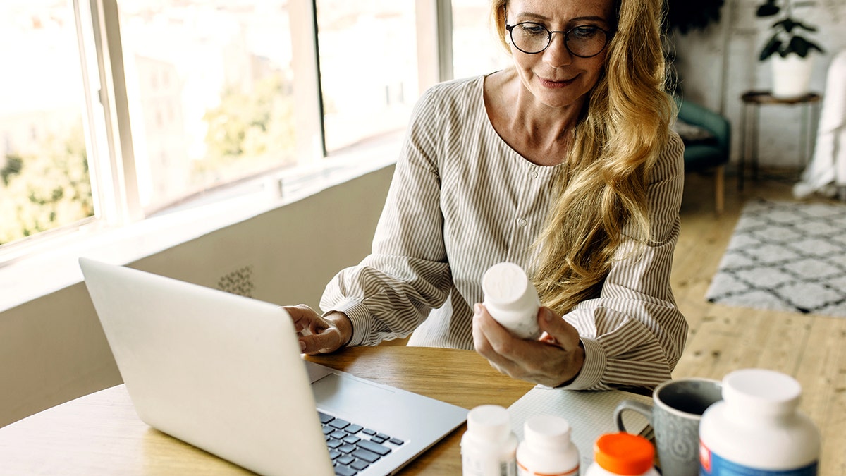 Woman looking at pill labels next to her computer