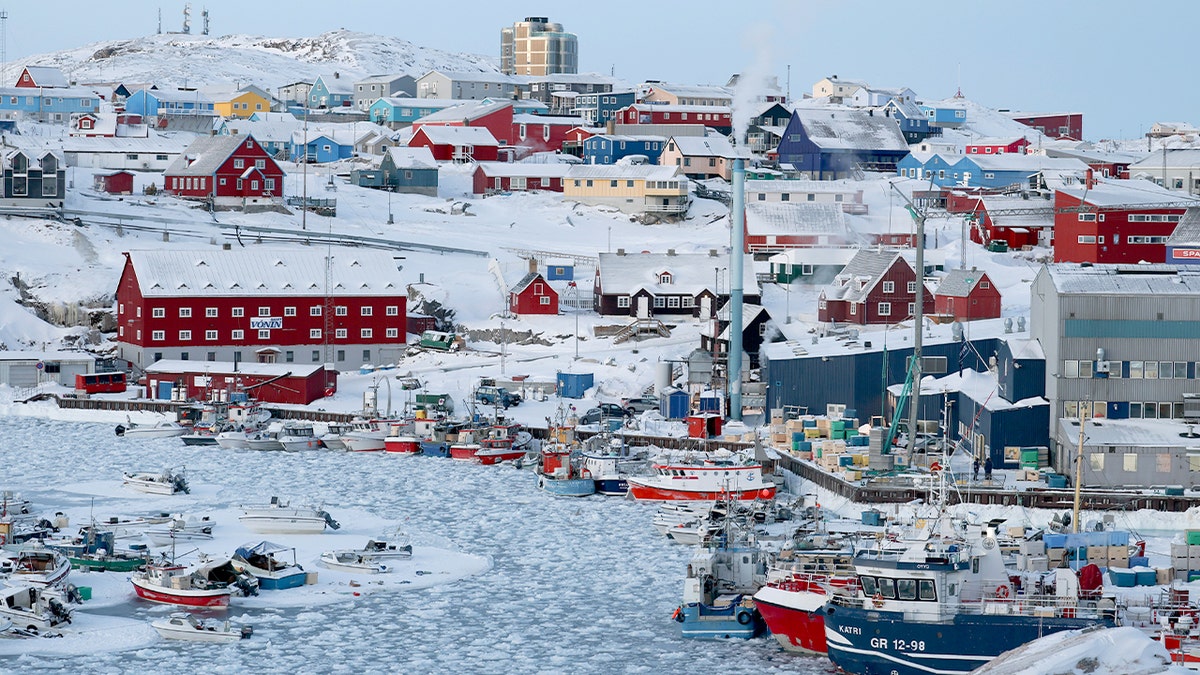 Sea ice forms a solid layer across a coastal harbor in a remote Arctic town.