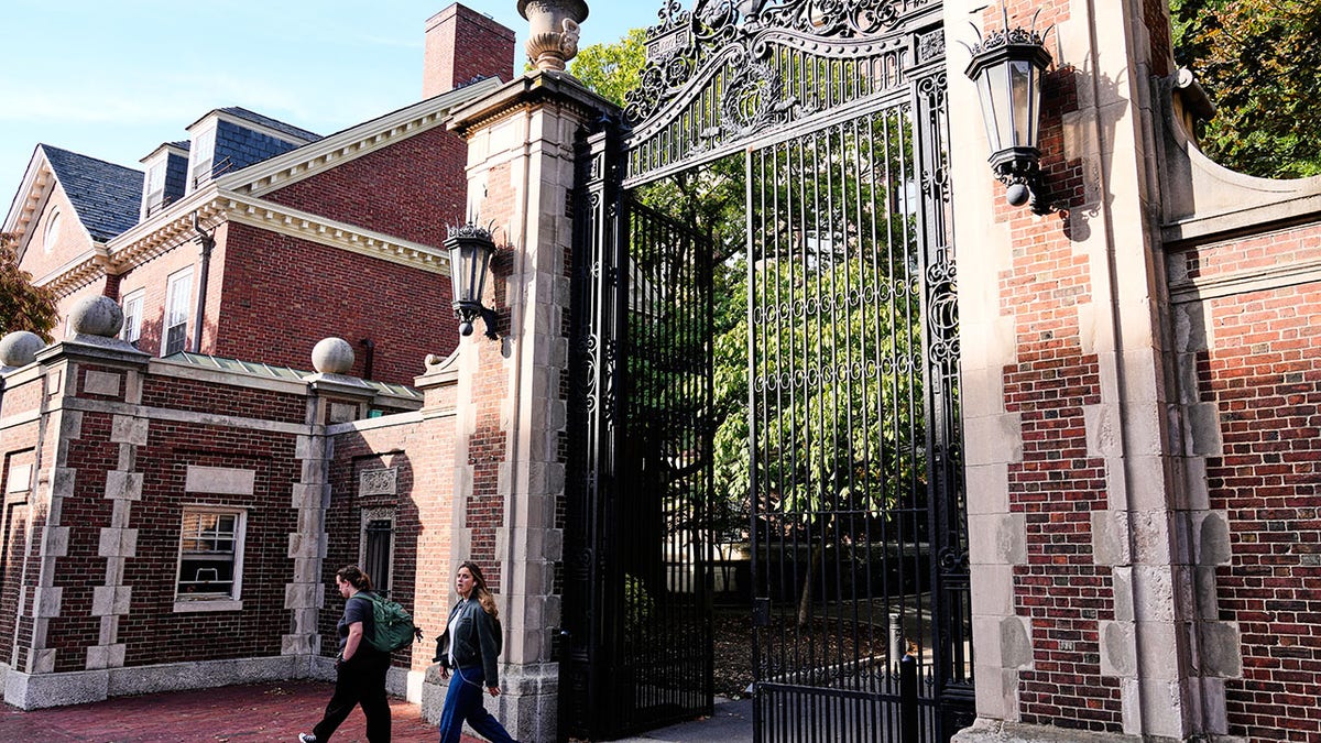 Harvard students walking through gate surrounded by brick wall and building
