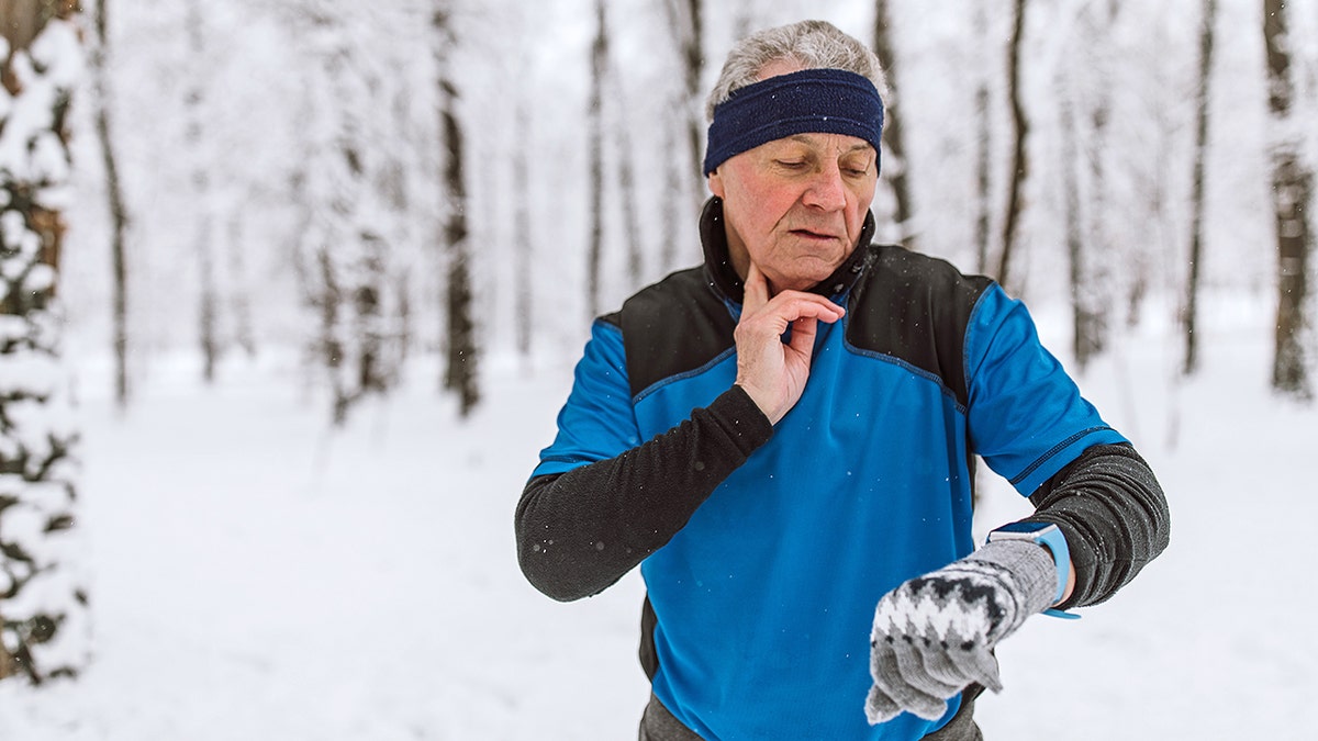 man feels pulse on neck with two fingers while outside in snow