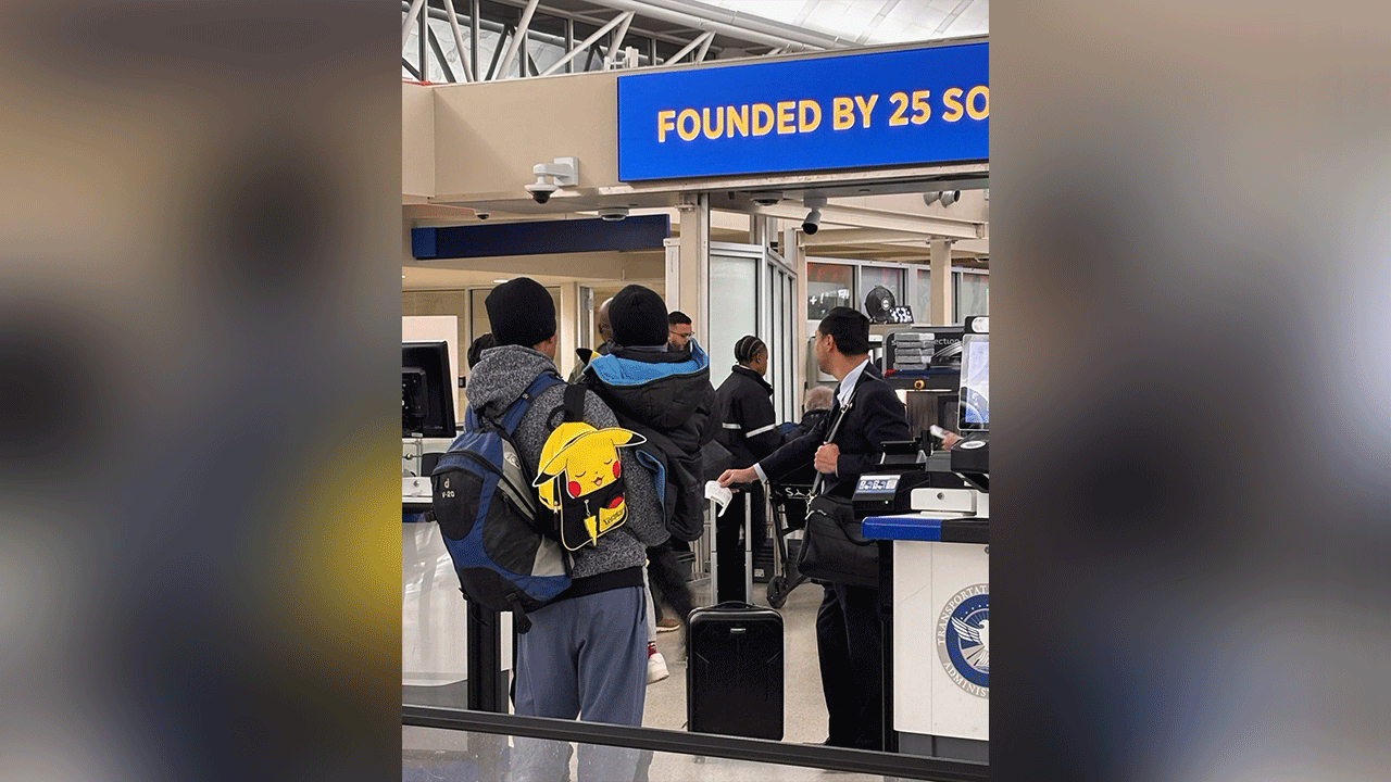 Adult and child stand with backpacks at an airport checkpoint.
