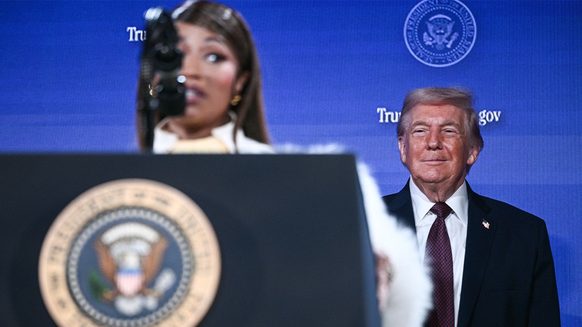 President Donald Trump stands smiling as Nicki Minaj speaks onstage at an event