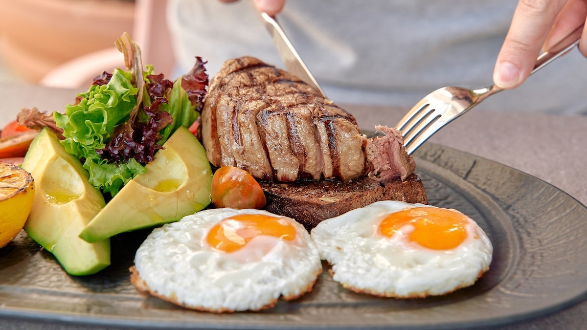 Person cutting steak with eggs on plate