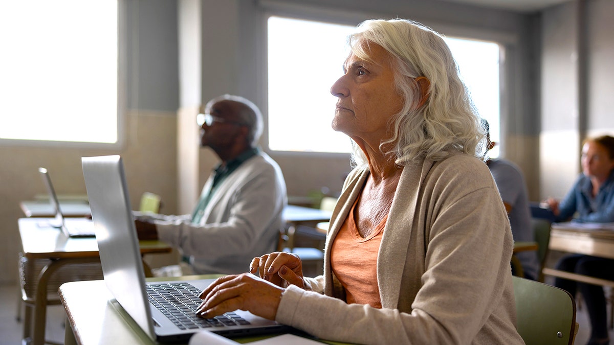 senior woman types on laptop in classroom