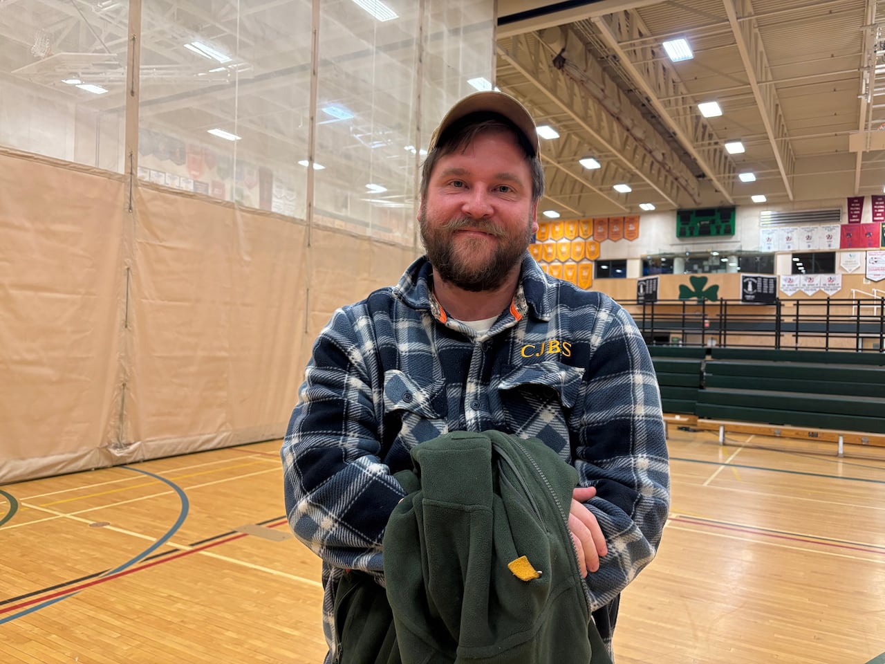 Mica Prazak, wearing a flannel shirt, stands in a school gym