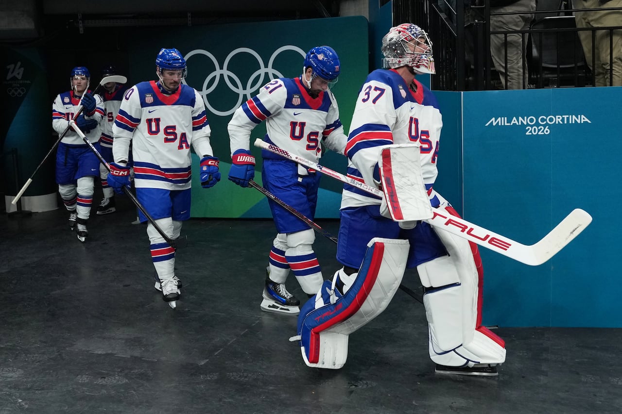 A Team USA goalie walks in an arena, followed by a row of teammates.