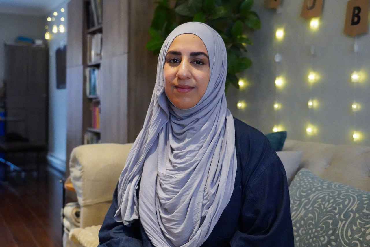 A woman in a hijab sits on a couch and smiles.