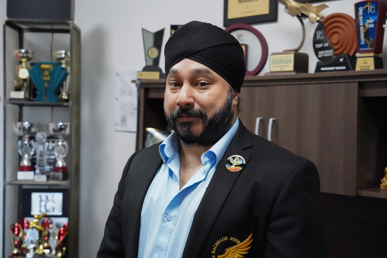 A man in a turban smiles in front of a trophy case.