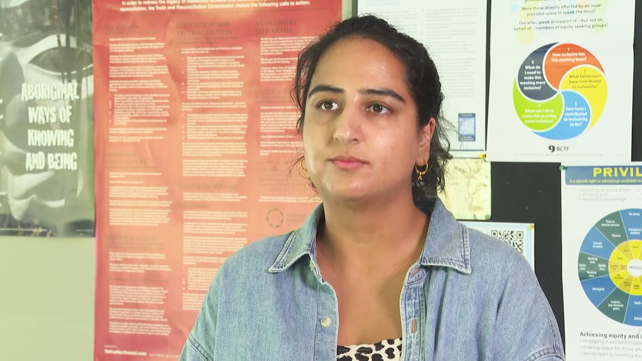 A woman with dark hair that's pulled back, wearing a denim button down over a black and white top.