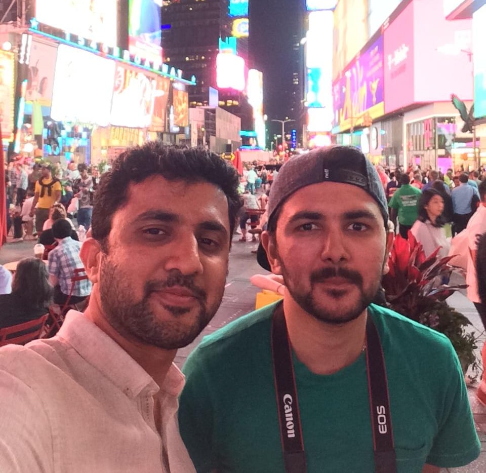 Two men standing in front of a busy city square smiling for a photo