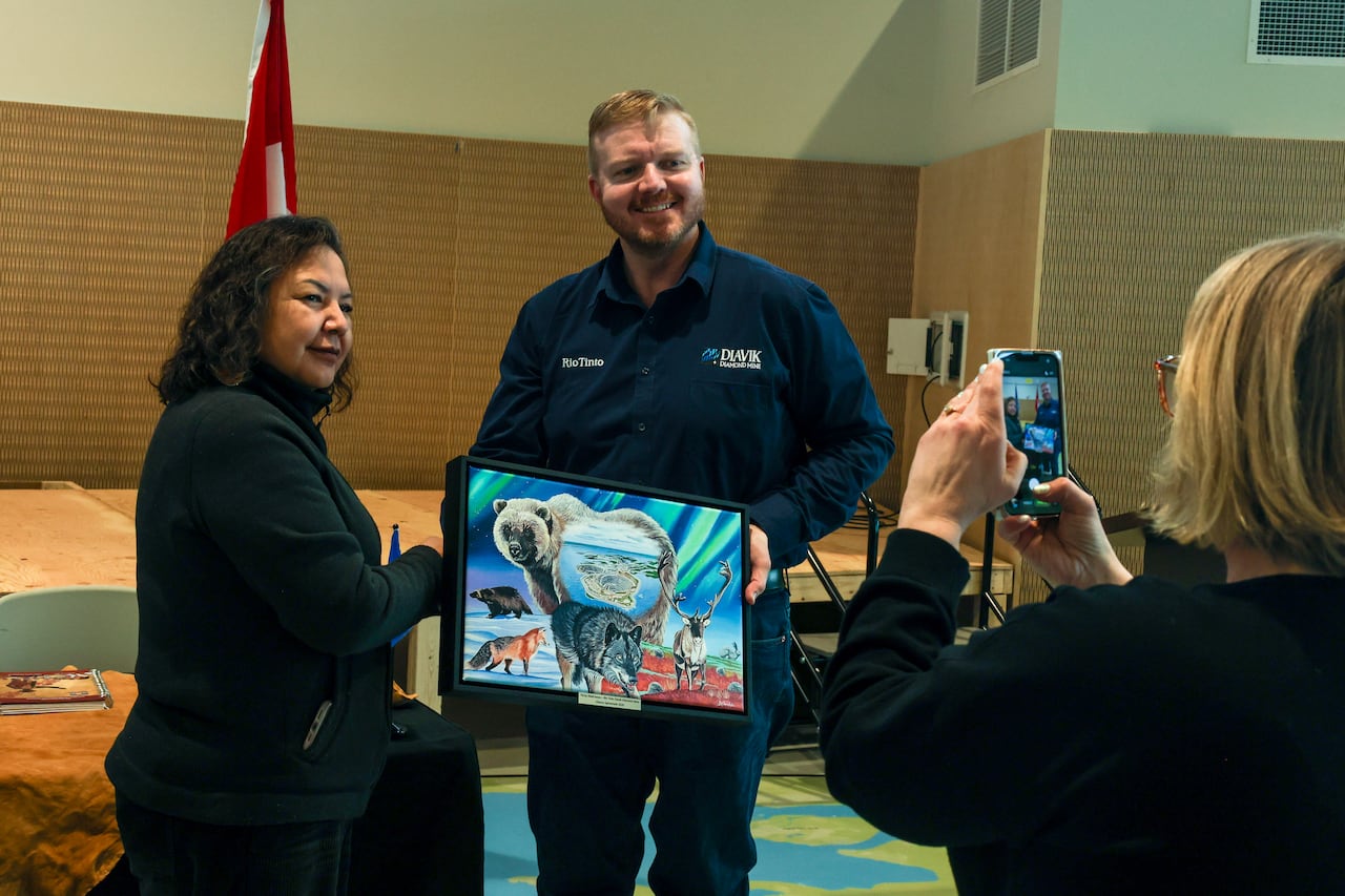 Two people stand holding a painting of various animals, with a diamond mine in the center 