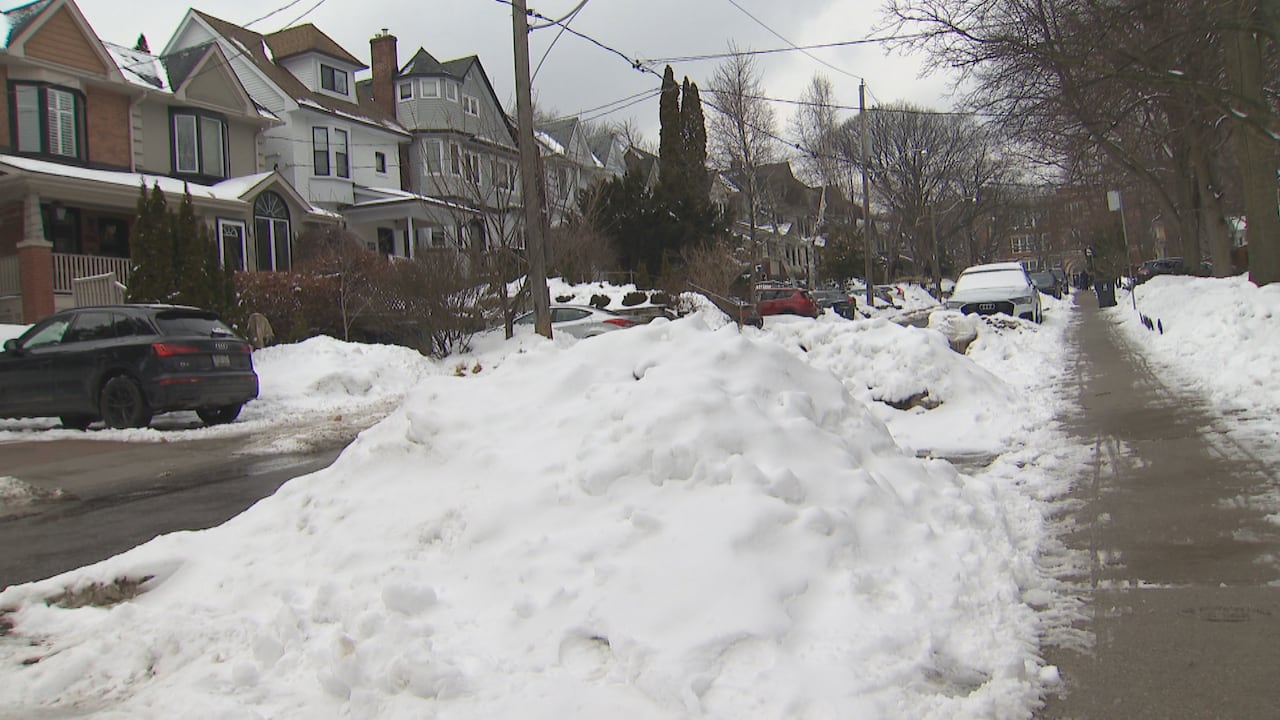 On Wineva Avenue near Queen Street East, the eastern side of the street is relatively clear but the western side remains covered by high snowbanks.