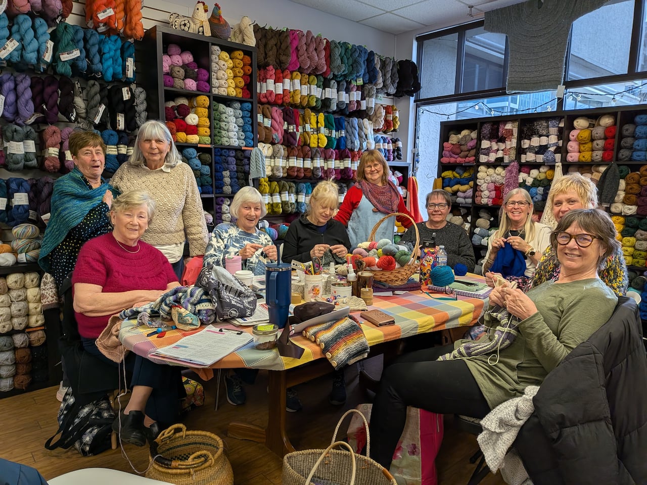 A group of people sit around a table knitting.