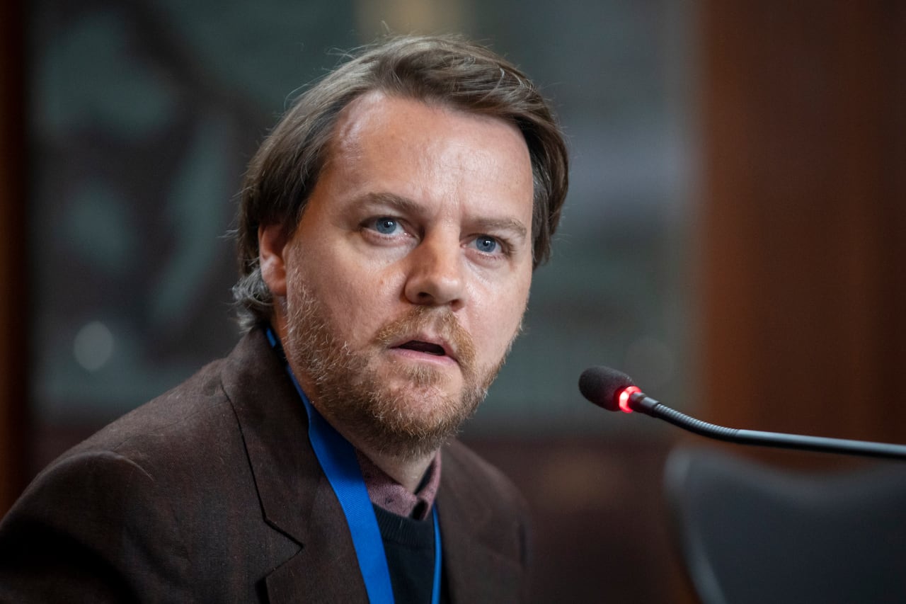 A bearded man speaks in front of a mic.