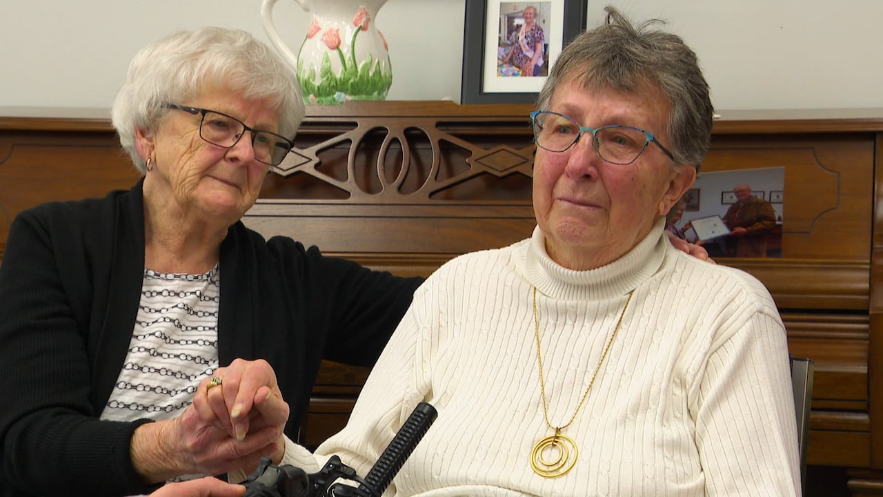 A woman holders the hand of another woman who is giving an emotional interview. 
