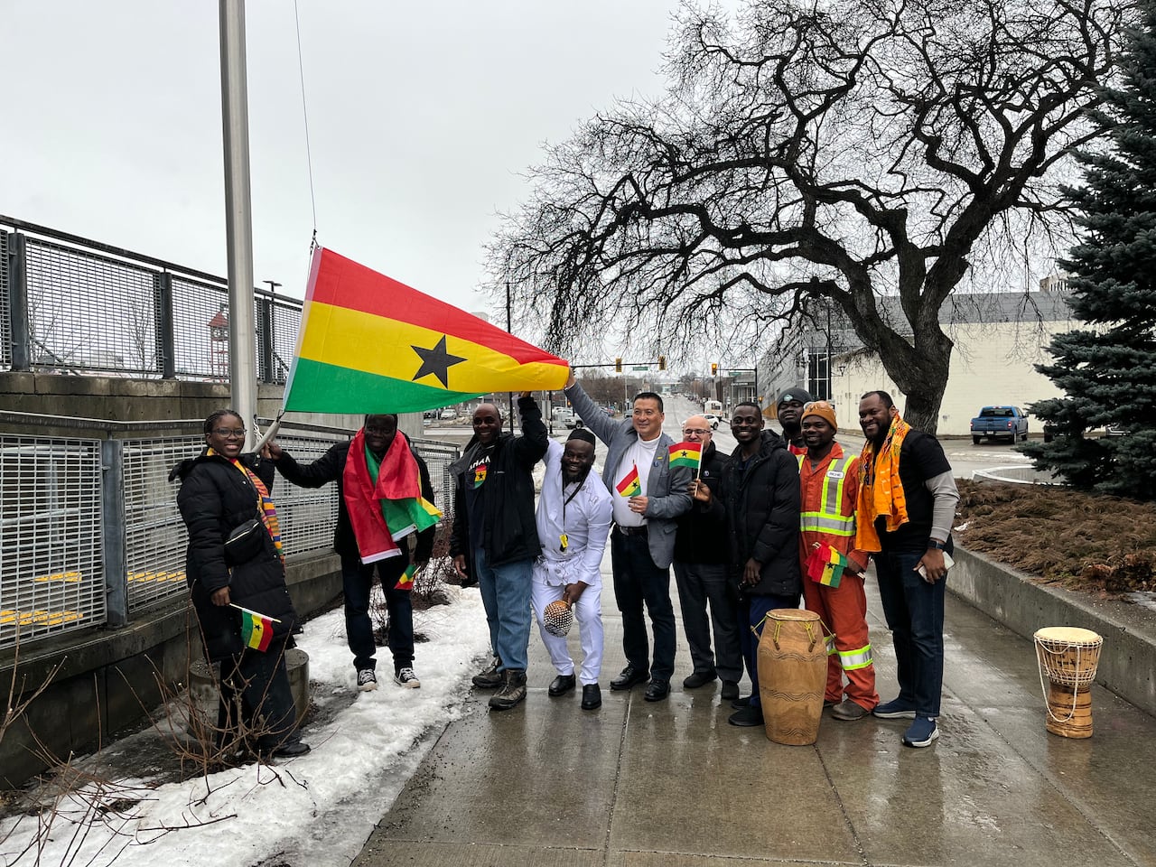A group of people hold out the Ghana flag as it sits at the base of a flag pole. 