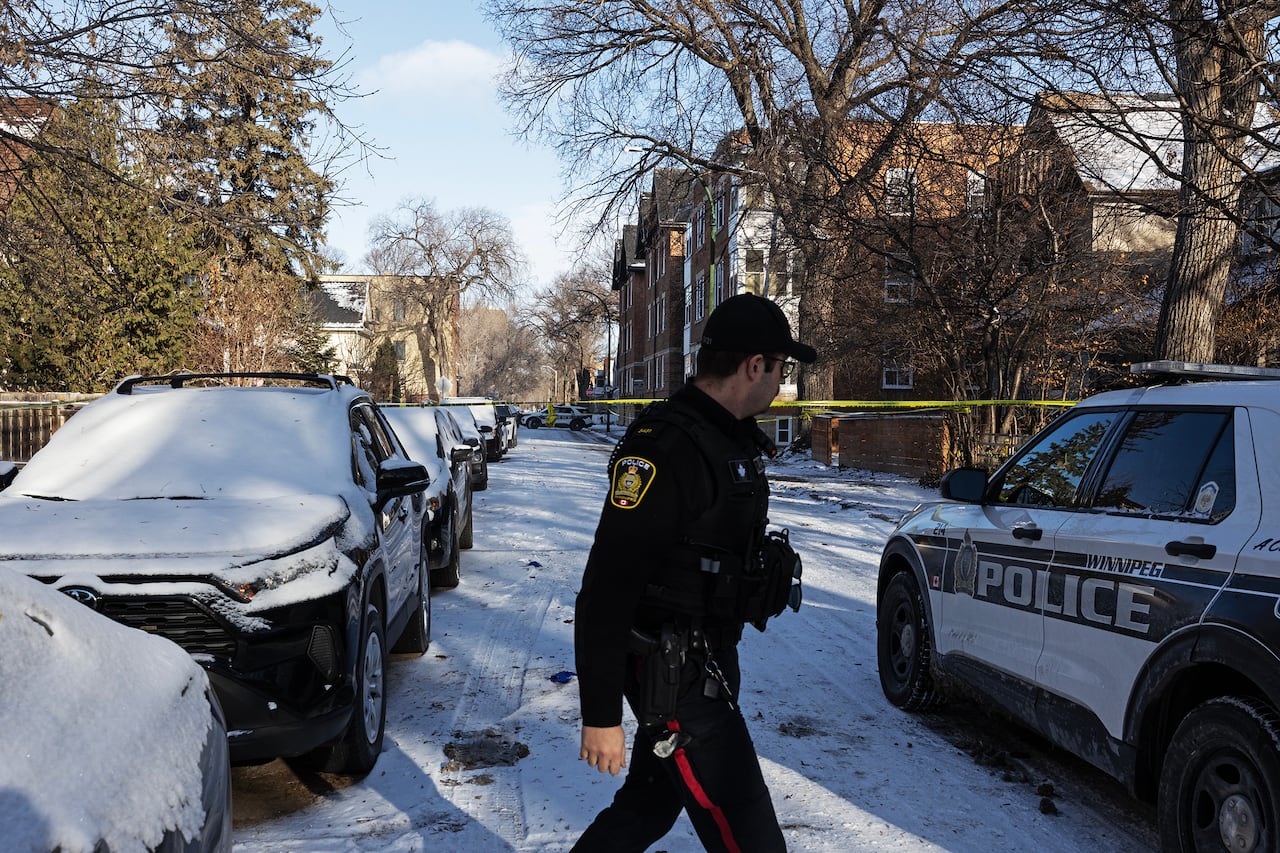A police officer walks on a street next to parked cars.