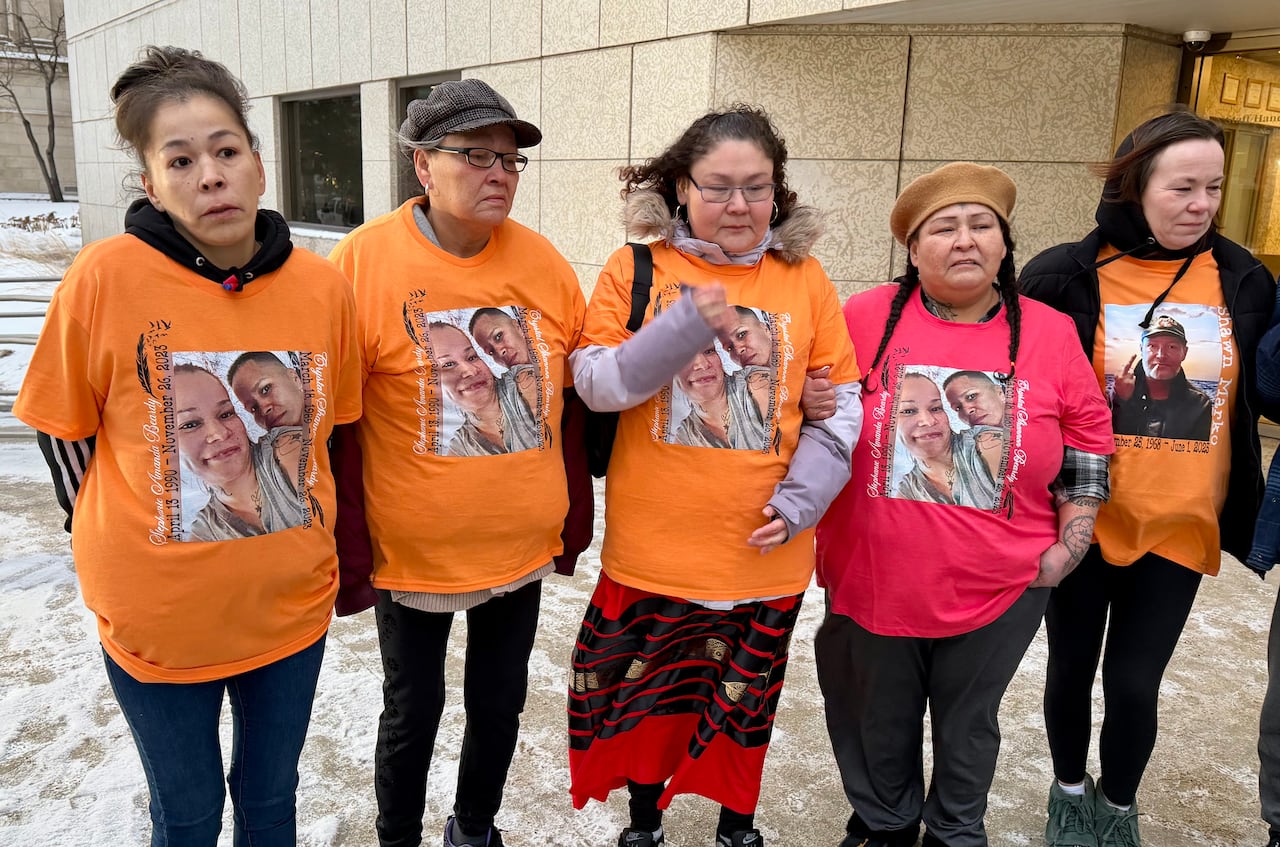 Five women wearing orange shirts with pictures on them stand in a line.